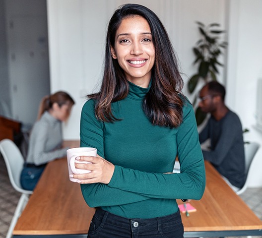 a young business professional holding a cup of coffee and crossing their arms