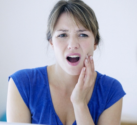 Woman in blue shirt with hand on cheek experiencing jaw pain