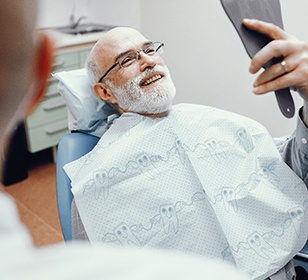 senior man beaming at his reflection after getting dental implants in Doylestown 