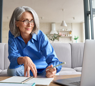 Woman taking notes while looking at laptop