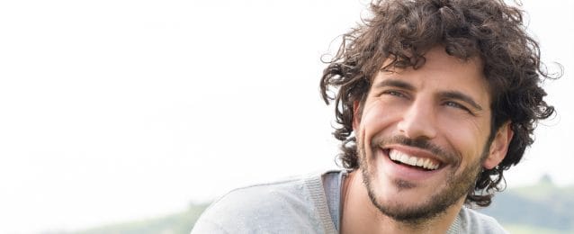 Man with curly hair smiling outside