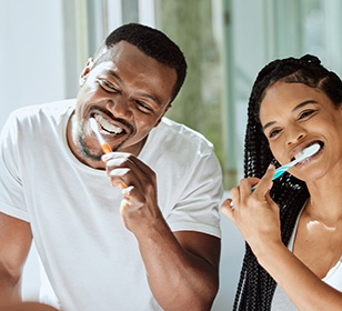 Couple smiling while brushing teeth together