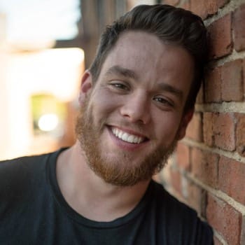 Bearded man smiling and leaning against brick wall