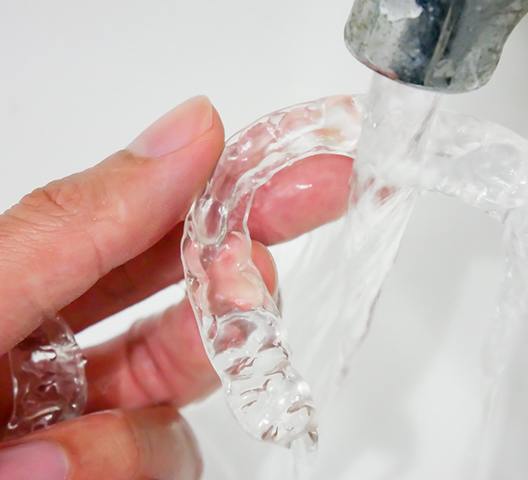 a person rinsing off their Invisalign aligners after earing