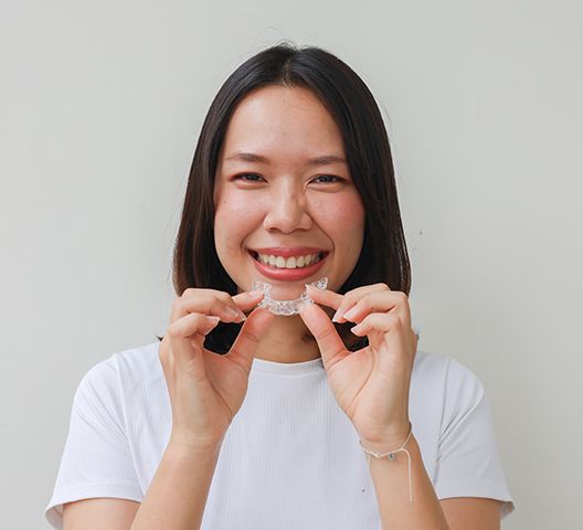 Teen girl smiling while holding clear aligner