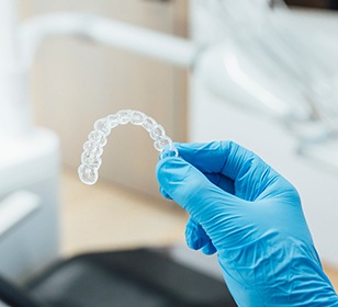 Dentist with blue glove holding clear aligner