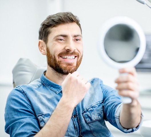 man smiling in mirror after smile makeover in Doylestown  