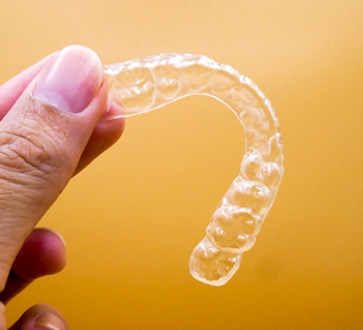 Close up of woman holding clear retainer with yellow background