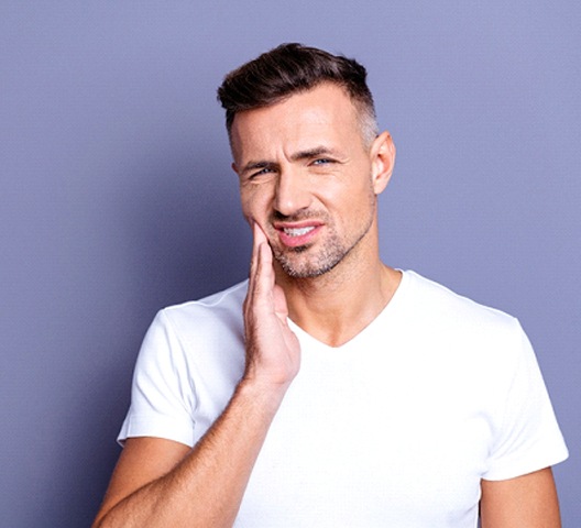 Man in white shirt with hand on cheek with jaw pain