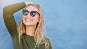 woman with sunglasses smiling after seeing her cosmetic dentist 