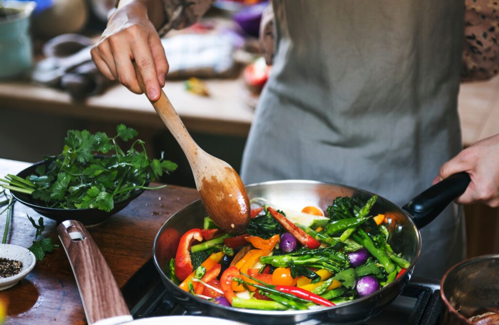 Closeup of someone in gray apron sautéing vegetables